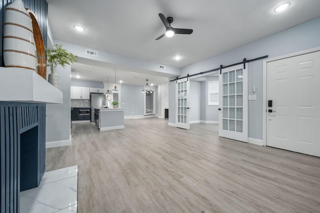 unfurnished living room featuring ceiling fan, a barn door, and light wood-type flooring