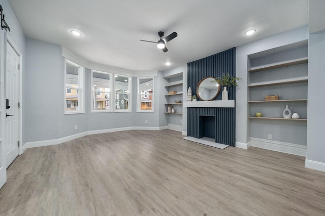 unfurnished living room with a fireplace, built in shelves, light hardwood / wood-style floors, and ceiling fan