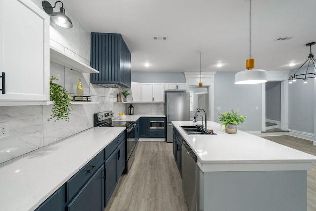 kitchen with blue cabinetry, appliances with stainless steel finishes, an island with sink, light hardwood / wood-style floors, and white cabinetry