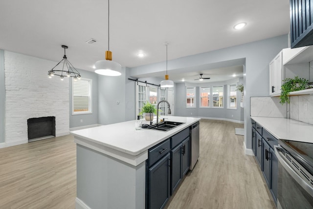 kitchen featuring appliances with stainless steel finishes, sink, light hardwood / wood-style floors, hanging light fixtures, and an island with sink