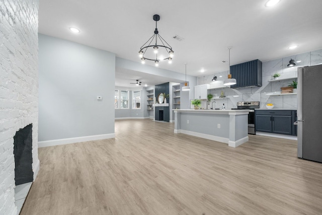 kitchen with ceiling fan with notable chandelier, decorative light fixtures, a fireplace, a center island with sink, and appliances with stainless steel finishes