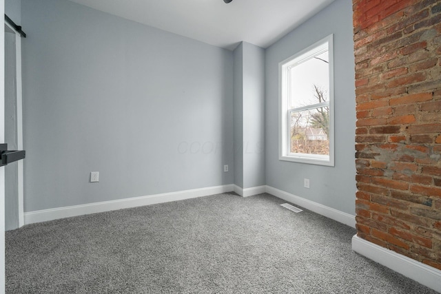 spare room featuring carpet flooring and brick wall