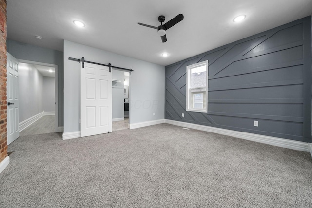 unfurnished bedroom featuring carpet, a barn door, and ceiling fan