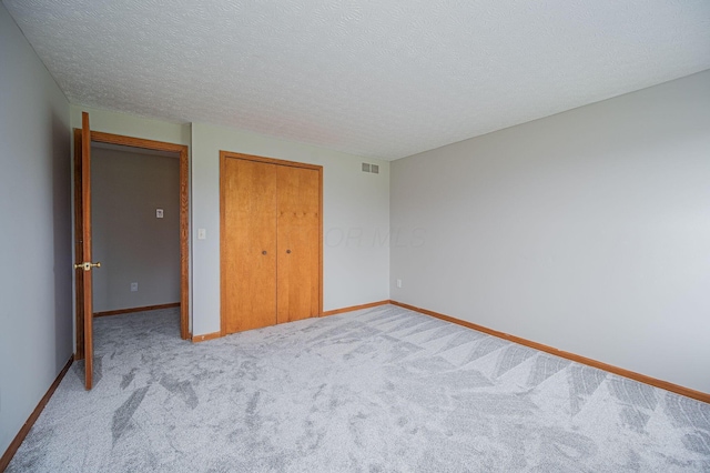 unfurnished bedroom with a textured ceiling, light carpet, and a closet