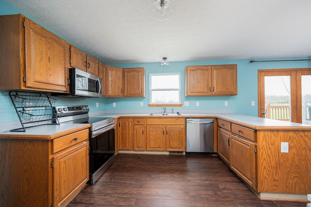 kitchen with kitchen peninsula, appliances with stainless steel finishes, a textured ceiling, dark wood-type flooring, and sink