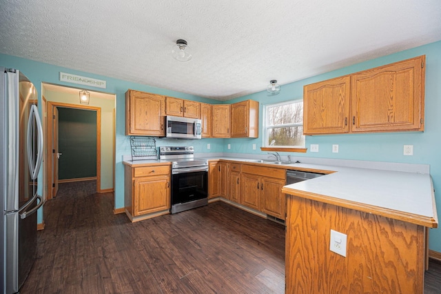 kitchen featuring kitchen peninsula, appliances with stainless steel finishes, dark hardwood / wood-style flooring, a textured ceiling, and sink