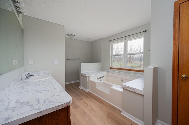 bathroom with hardwood / wood-style flooring, vanity, a tub to relax in, and a textured ceiling