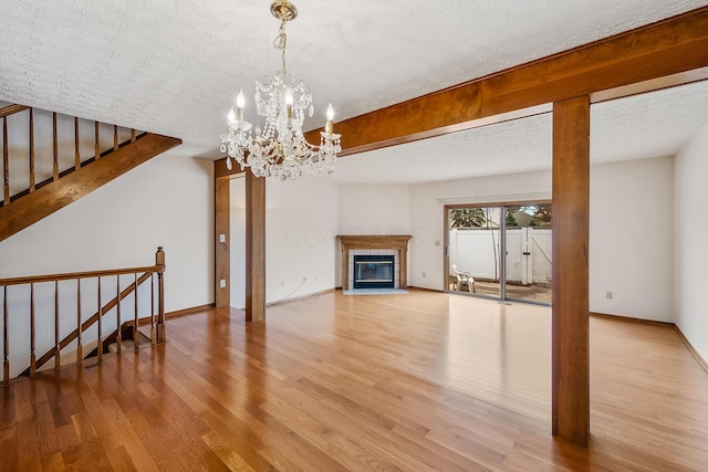 living room with a tile fireplace, a textured ceiling, a chandelier, and light hardwood / wood-style flooring