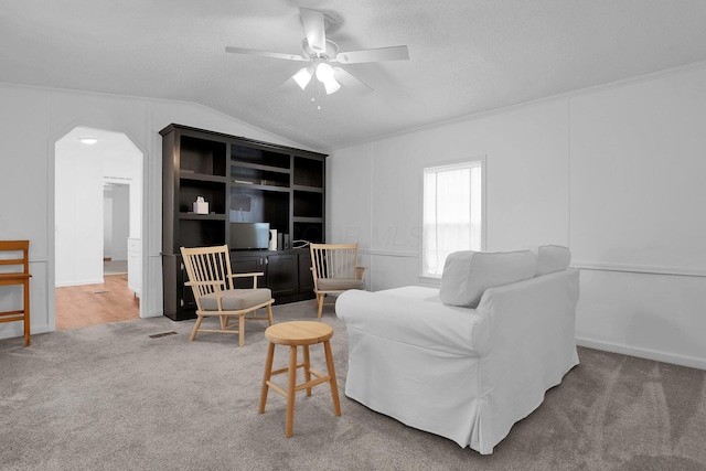 carpeted living room featuring a textured ceiling, ceiling fan, vaulted ceiling, and ornamental molding