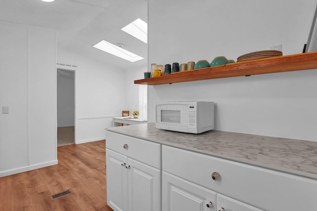 kitchen featuring white cabinetry, light wood-type flooring, and lofted ceiling with skylight