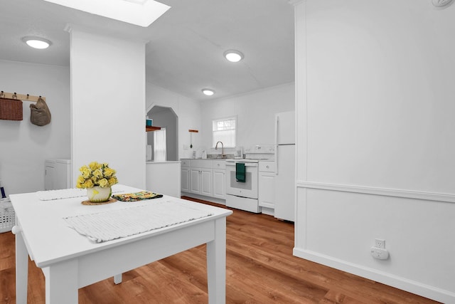 kitchen featuring a skylight, white cabinetry, sink, light hardwood / wood-style floors, and white appliances