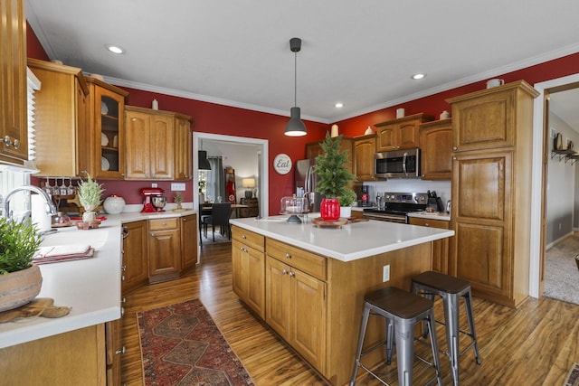 kitchen with stainless steel appliances, wood-type flooring, pendant lighting, a kitchen island, and crown molding