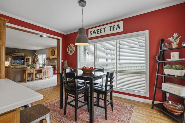 dining area featuring hardwood / wood-style floors, ornamental molding, and a stone fireplace