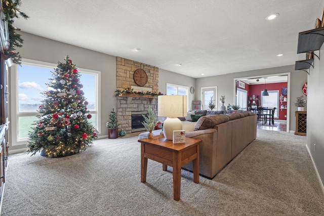 carpeted living room with a textured ceiling, a wealth of natural light, a water view, and a stone fireplace