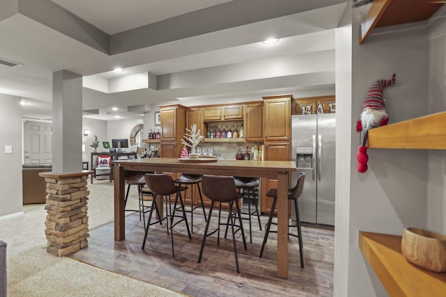 kitchen featuring a kitchen bar, tasteful backsplash, stainless steel fridge, dark hardwood / wood-style floors, and kitchen peninsula