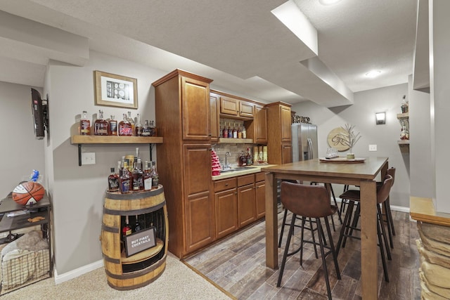 bar featuring sink, backsplash, stainless steel fridge, and light hardwood / wood-style flooring