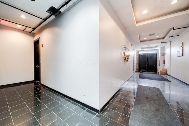 corridor with a tray ceiling and dark tile patterned flooring