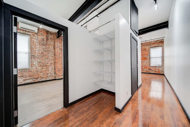 hall with a wall mounted air conditioner, hardwood / wood-style flooring, and brick wall