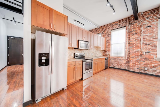 kitchen with appliances with stainless steel finishes, light hardwood / wood-style flooring, beam ceiling, and brick wall