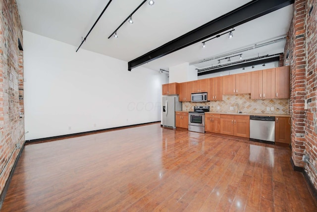 kitchen with sink, dark wood-type flooring, stainless steel appliances, brick wall, and decorative backsplash