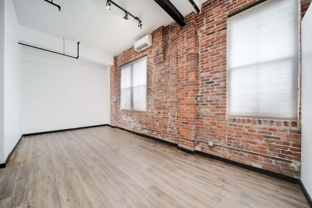 unfurnished room featuring a wall mounted air conditioner, beam ceiling, brick wall, and light hardwood / wood-style flooring