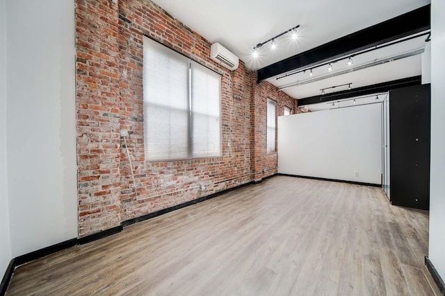 unfurnished room with beam ceiling, rail lighting, brick wall, a wall unit AC, and wood-type flooring