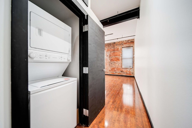 laundry room with stacked washer and dryer, hardwood / wood-style flooring, and brick wall