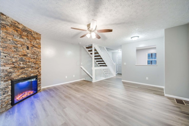 unfurnished living room featuring a textured ceiling, hardwood / wood-style flooring, a stone fireplace, and ceiling fan