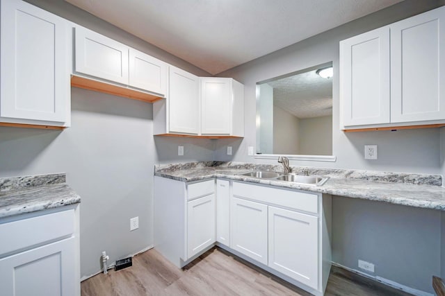 kitchen featuring a textured ceiling, light hardwood / wood-style floors, white cabinetry, and sink