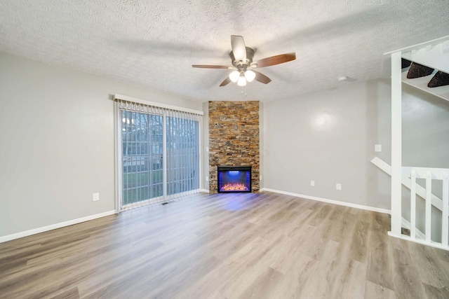 unfurnished living room with a textured ceiling, light hardwood / wood-style flooring, ceiling fan, and a stone fireplace