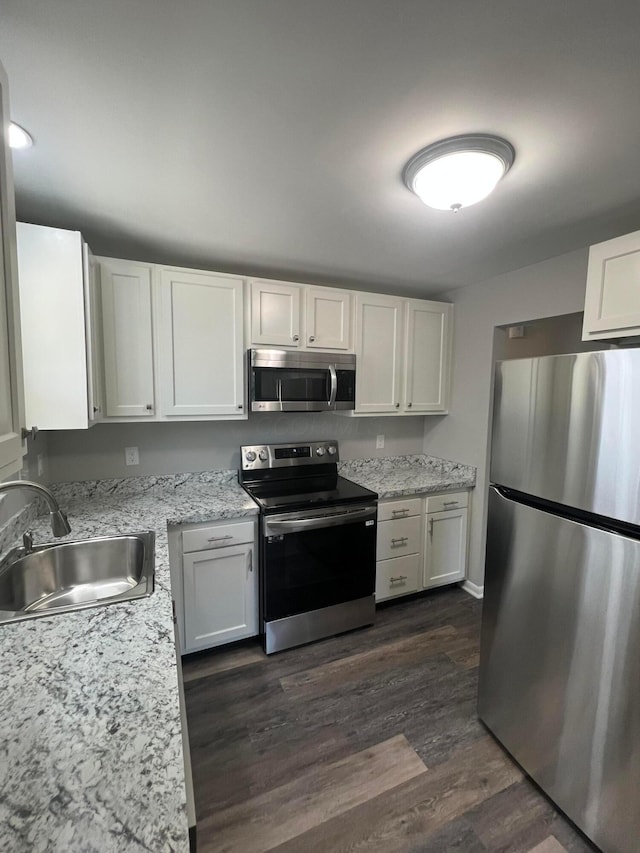 kitchen with dark wood-type flooring, a sink, white cabinetry, appliances with stainless steel finishes, and light stone countertops