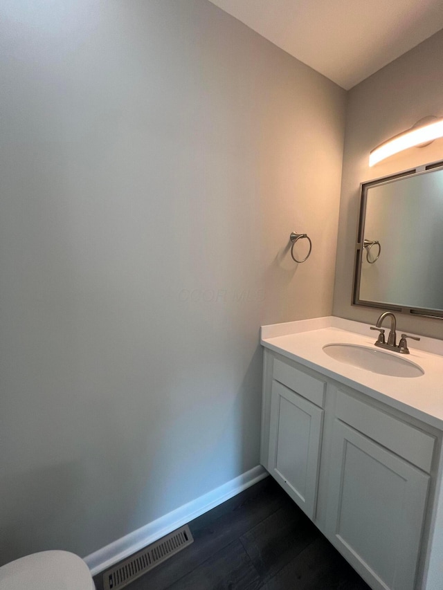 bathroom with baseboards, visible vents, toilet, wood finished floors, and vanity