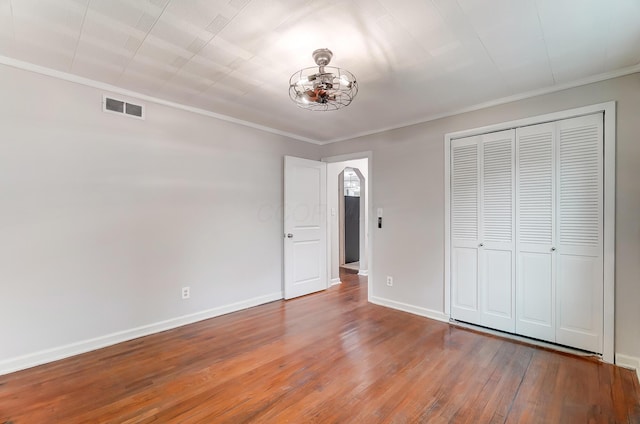 unfurnished bedroom with crown molding, an inviting chandelier, hardwood / wood-style floors, and a closet