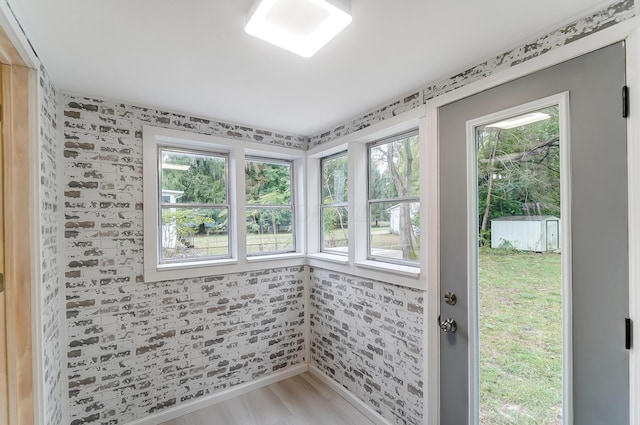 doorway to outside with light hardwood / wood-style flooring and brick wall