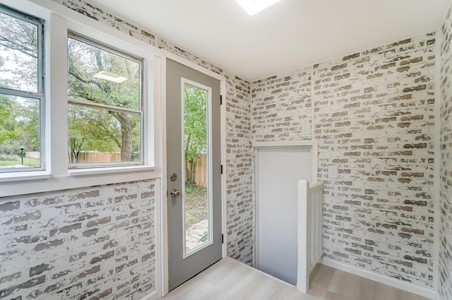 doorway to outside with brick wall and light hardwood / wood-style flooring