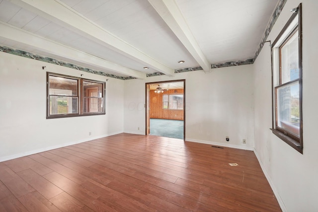 empty room featuring beamed ceiling, plenty of natural light, and hardwood / wood-style flooring