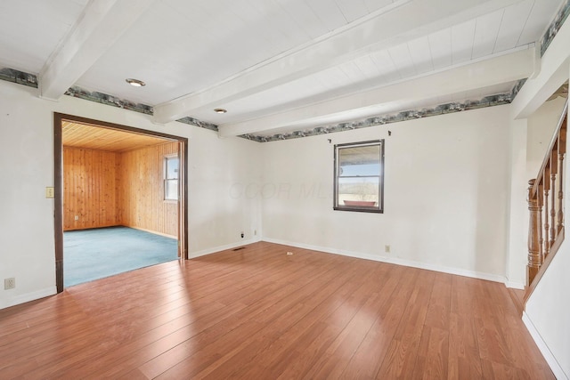 empty room featuring wood walls, light wood-type flooring, and beam ceiling