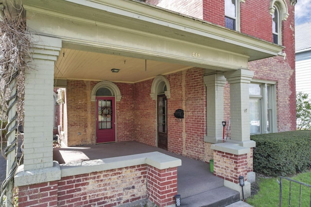 entrance to property with a porch and brick siding