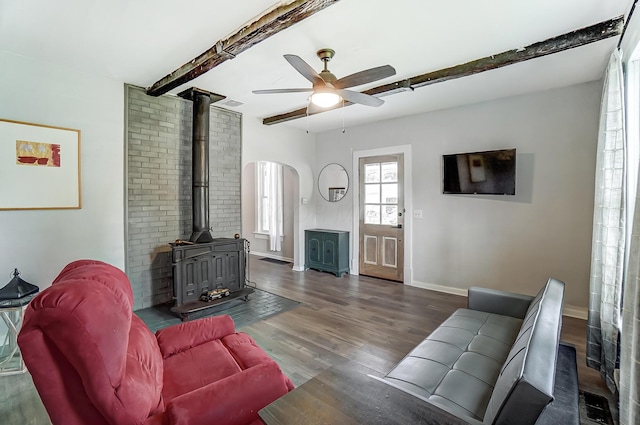 living room with beamed ceiling, ceiling fan, dark hardwood / wood-style flooring, and a wood stove