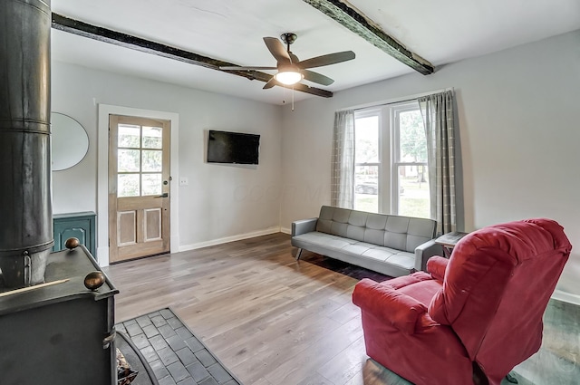 living room featuring a healthy amount of sunlight, beam ceiling, light hardwood / wood-style flooring, and a wood stove