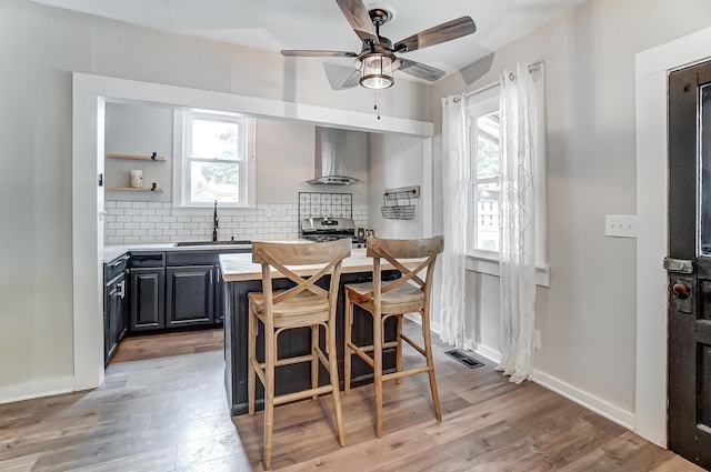 kitchen with sink, a kitchen breakfast bar, decorative backsplash, light hardwood / wood-style floors, and wall chimney exhaust hood