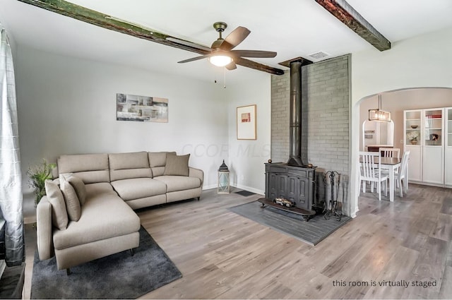 living room featuring beamed ceiling, hardwood / wood-style flooring, a wood stove, and ceiling fan