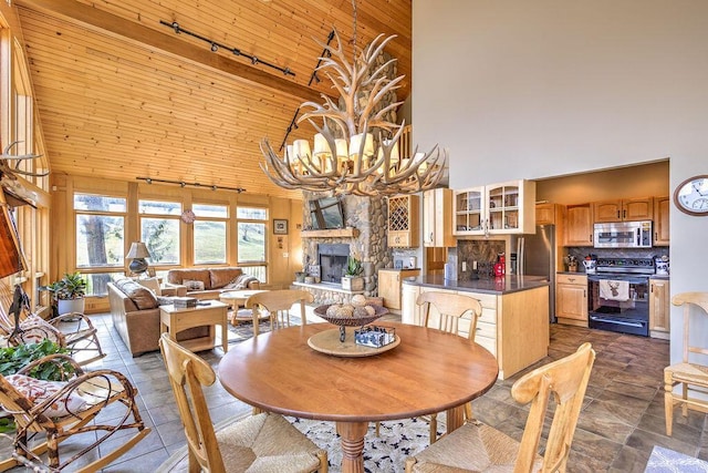 dining area featuring beamed ceiling, wooden ceiling, a chandelier, a high ceiling, and a stone fireplace