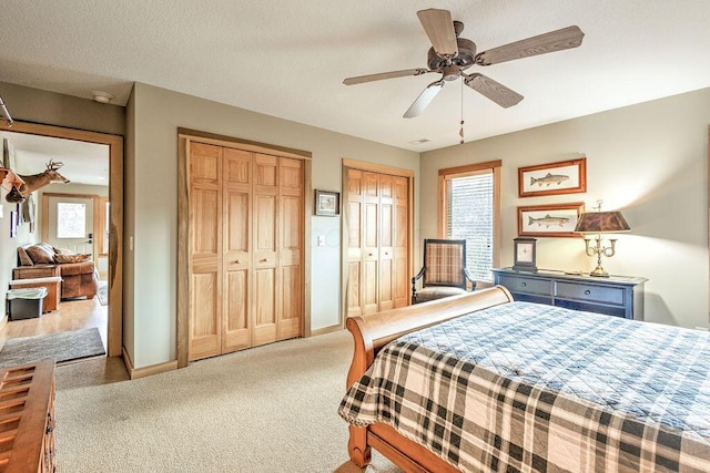 carpeted bedroom with a textured ceiling, multiple windows, ceiling fan, and multiple closets