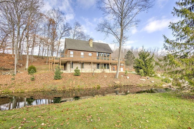 rear view of property featuring a deck with water view and a lawn