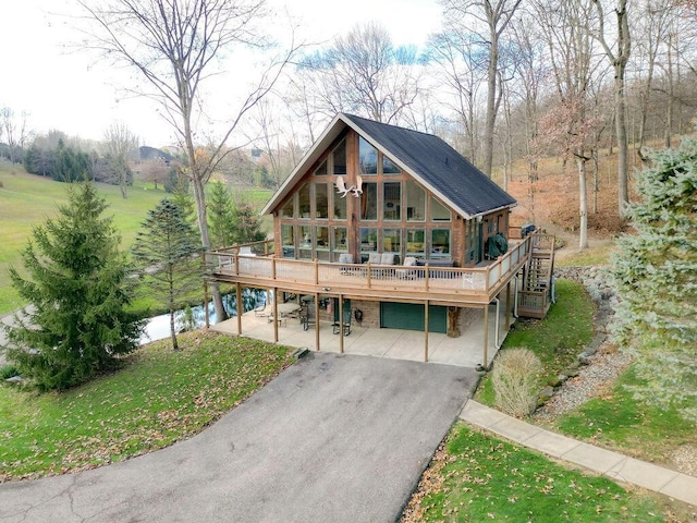 back of house with a lawn, a deck with water view, and a garage