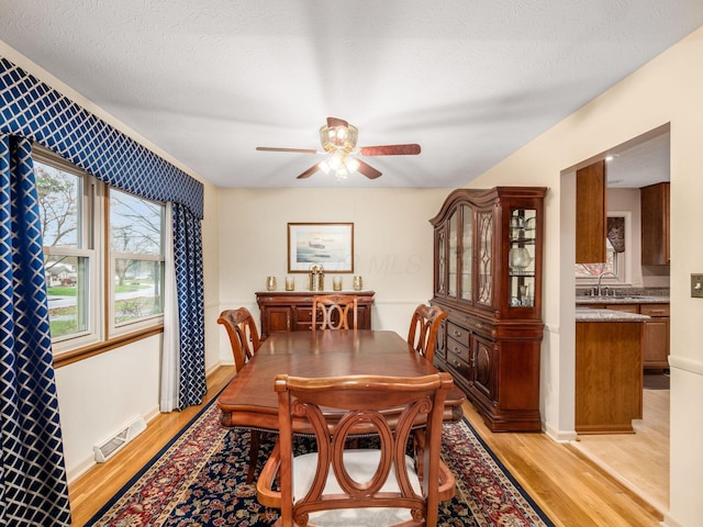 dining space with ceiling fan, sink, a textured ceiling, and light hardwood / wood-style flooring