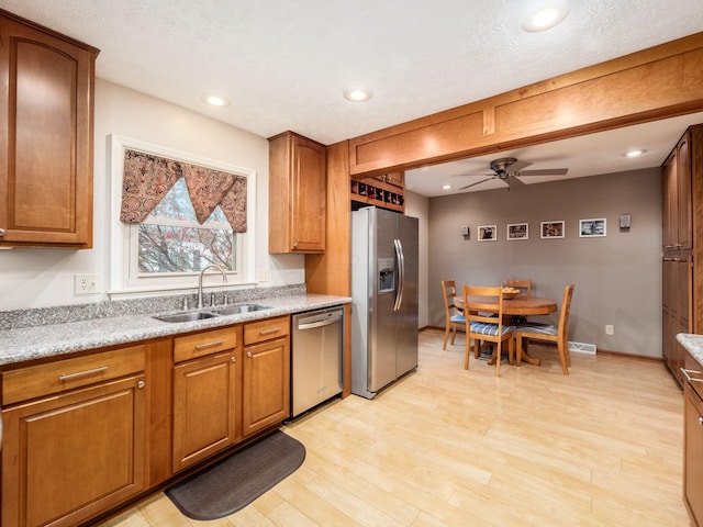 kitchen featuring appliances with stainless steel finishes, light wood-type flooring, light stone counters, ceiling fan, and sink