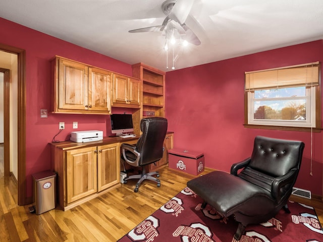 office space featuring wood-type flooring, built in desk, and ceiling fan