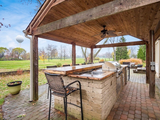 view of patio featuring ceiling fan, area for grilling, exterior bar, and a grill